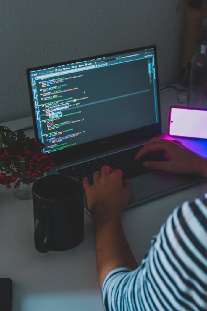 A person coding on a laptop in a home office setting with ambient lighting.